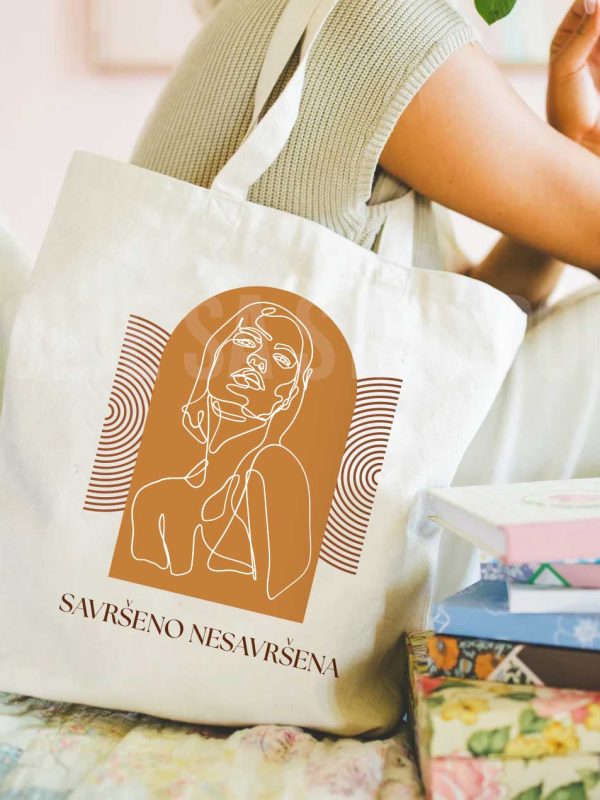 Ceger sa natpisom savrseno nesavrsena, devojka sedi i nosi ga na ramenu, oko nje knjige
